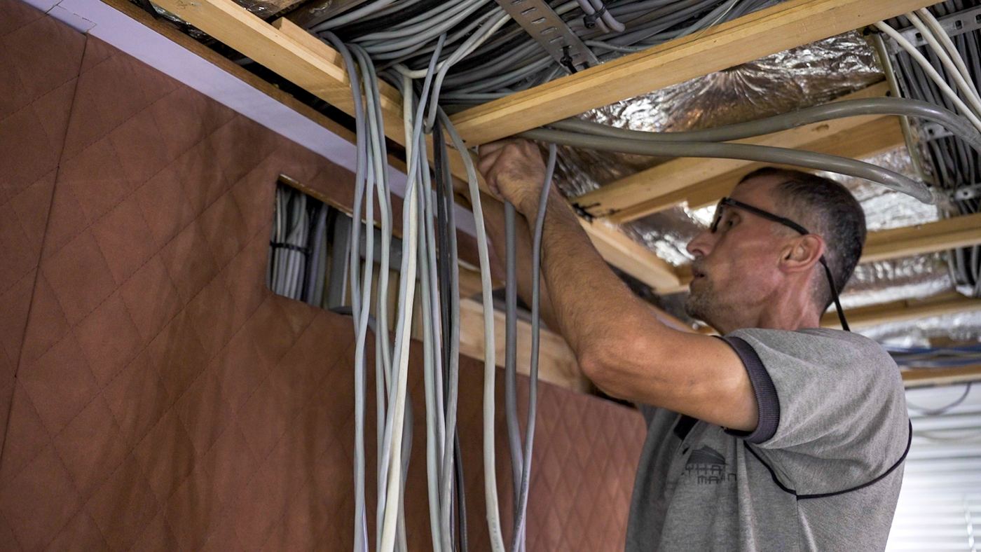 An electrician running cable looms above an opened panel inside the yacht
