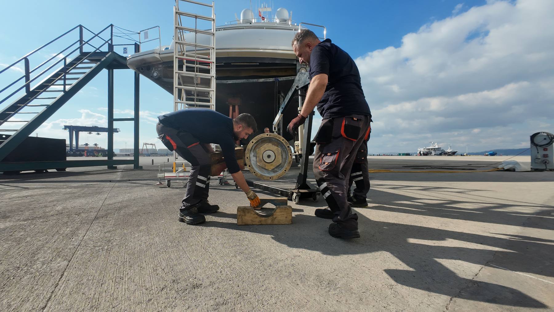 Yard team handling a mechanical component beside a motor yacht in Tuzla